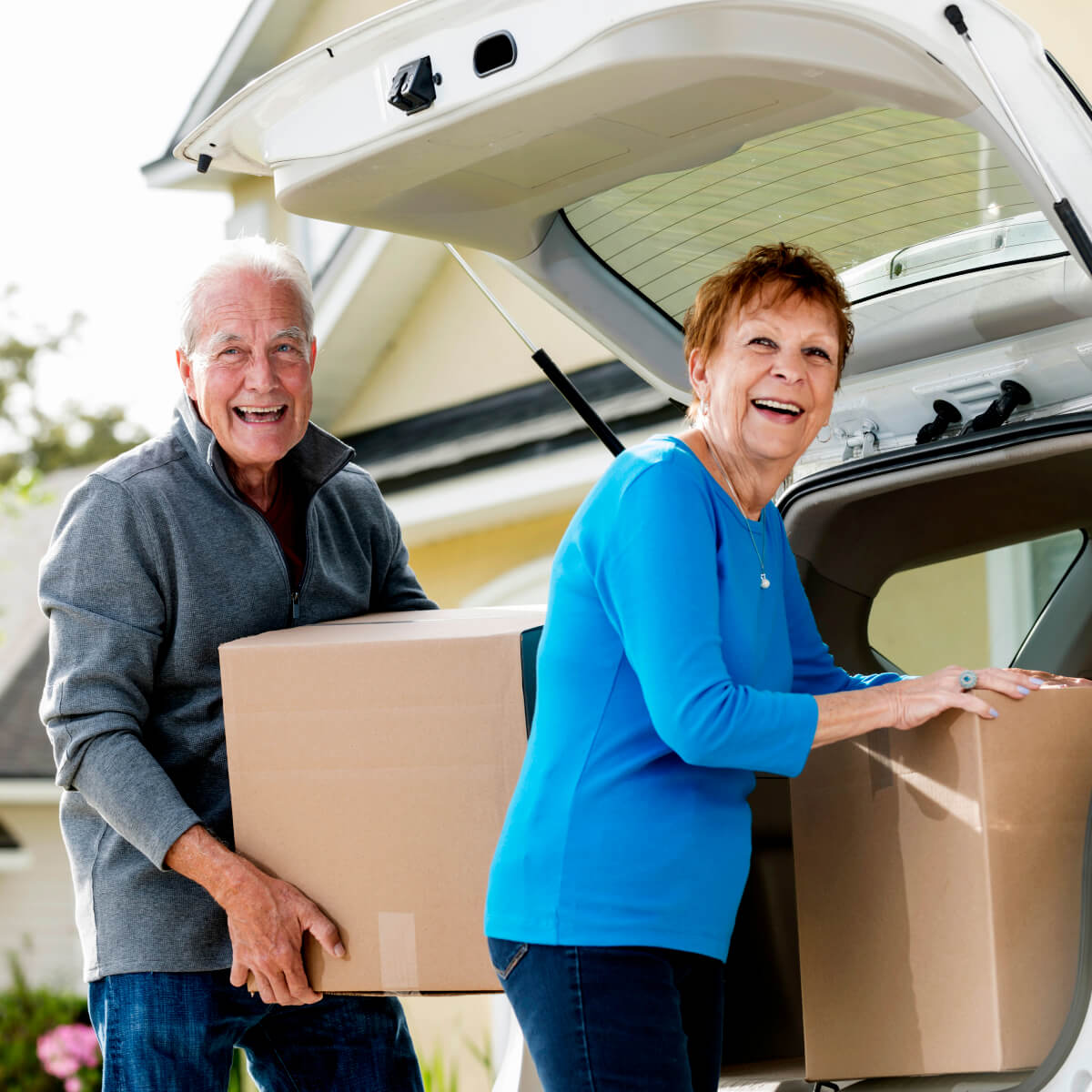 Senior couple loading or unloading boxes from the trunk of their car parked in front of the house
